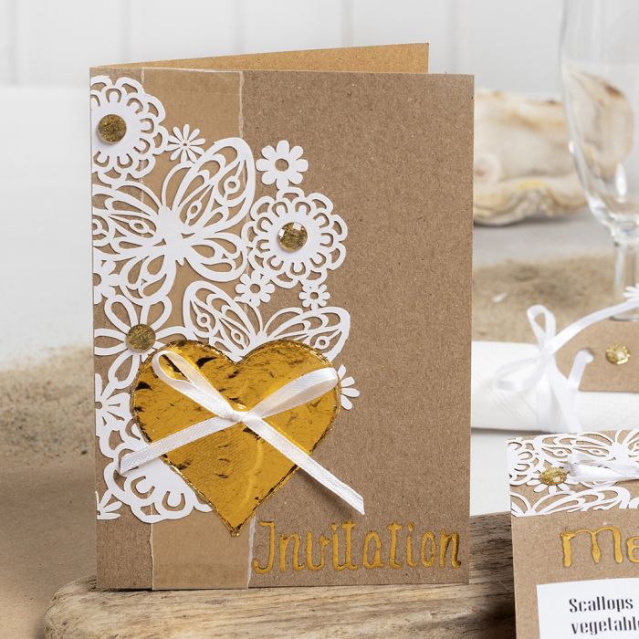 Une invitation décorée avec du carton à motif de dentelle, un cœur en feuille décorative et des strass