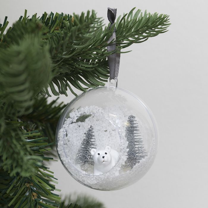 Une boule de Noël avec un trou à l’avant, décorée de neige artificielle et de mini figurines