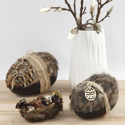 Un œuf en papier mâché en deux parties décoré de plumes naturelles et de ficelle naturelle.