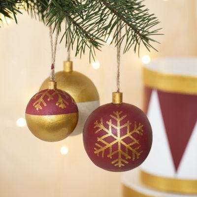 Des boules de Noël en bois décorées avec de la peinture acrylique et des feutres Plus Color